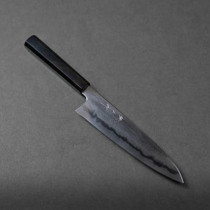 A Japanese chef’s knife with a dark wooden handle and a beautifully patterned steel blade rests diagonally on a gray surface. Intricate Japanese characters are engraved on the blade, highlighting its authentic craftsmanship.