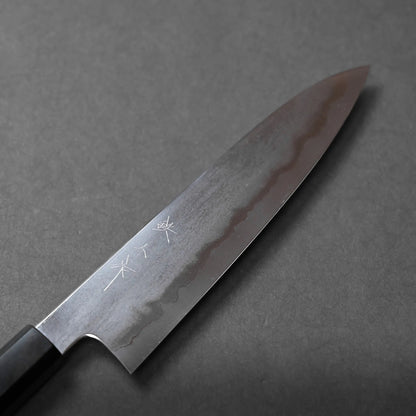 A Japanese chef’s knife with a dark handle and Damascus steel blade rests on a grey surface. The blade displays a wavy pattern and engraved kanji characters, highlighting traditional craftsmanship.