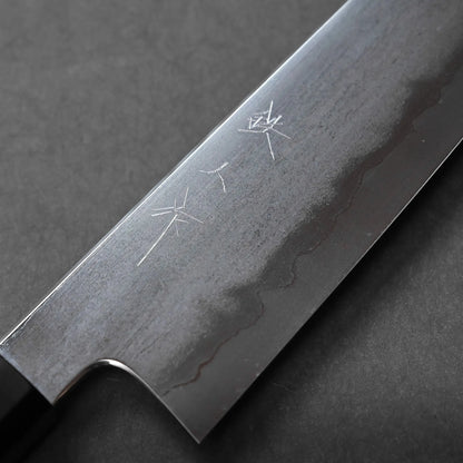 Close-up of a Japanese kitchen knife blade featuring a wavy Damascus pattern and engraved kanji characters, set against a dark, textured background.