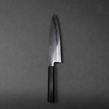 A single Japanese chef’s knife with a dark wooden handle and a slightly reflective blade rests on a plain, dark gray background.