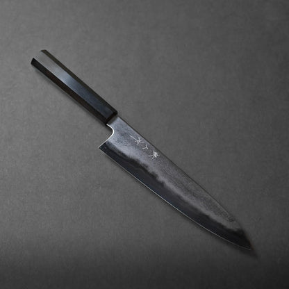 A Japanese chef’s knife with a dark handle and blade, featuring a subtle wavy Damascus pattern and Japanese characters engraved near the spine, displayed on a dark gray background.