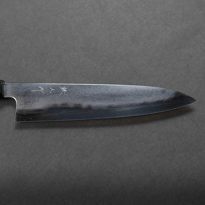A close-up view of a Japanese-style kitchen knife with a dark, polished blade featuring subtle engravings, placed against a textured background that highlights its Japanese craftsmanship.