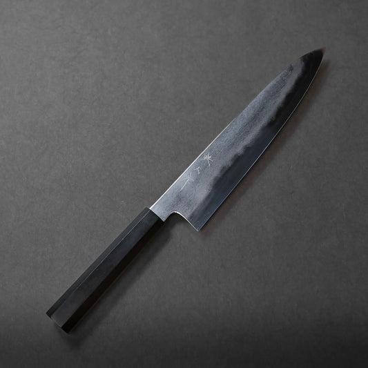 A Tetsujin tanryusen ginsan gyuto 240mm with a dark blade and hexagonal handle rests on a dark grey surface, photographed from above, showcasing its traditional craftsmanship.
