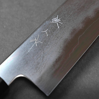 Close-up of a steel knife blade featuring Japanese characters engraved on its surface, set against a dark, matte background. The knife displays a visible edge and a partial black handle.