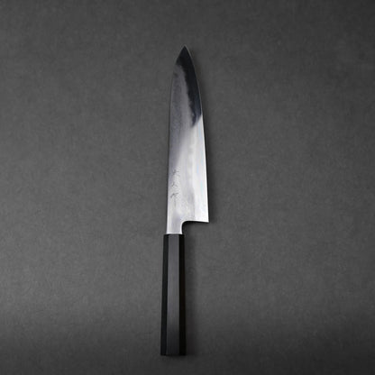A chef's knife with a shiny, reflective blade and a black handle rests on a dark gray surface, photographed from above for a sleek, professional look.