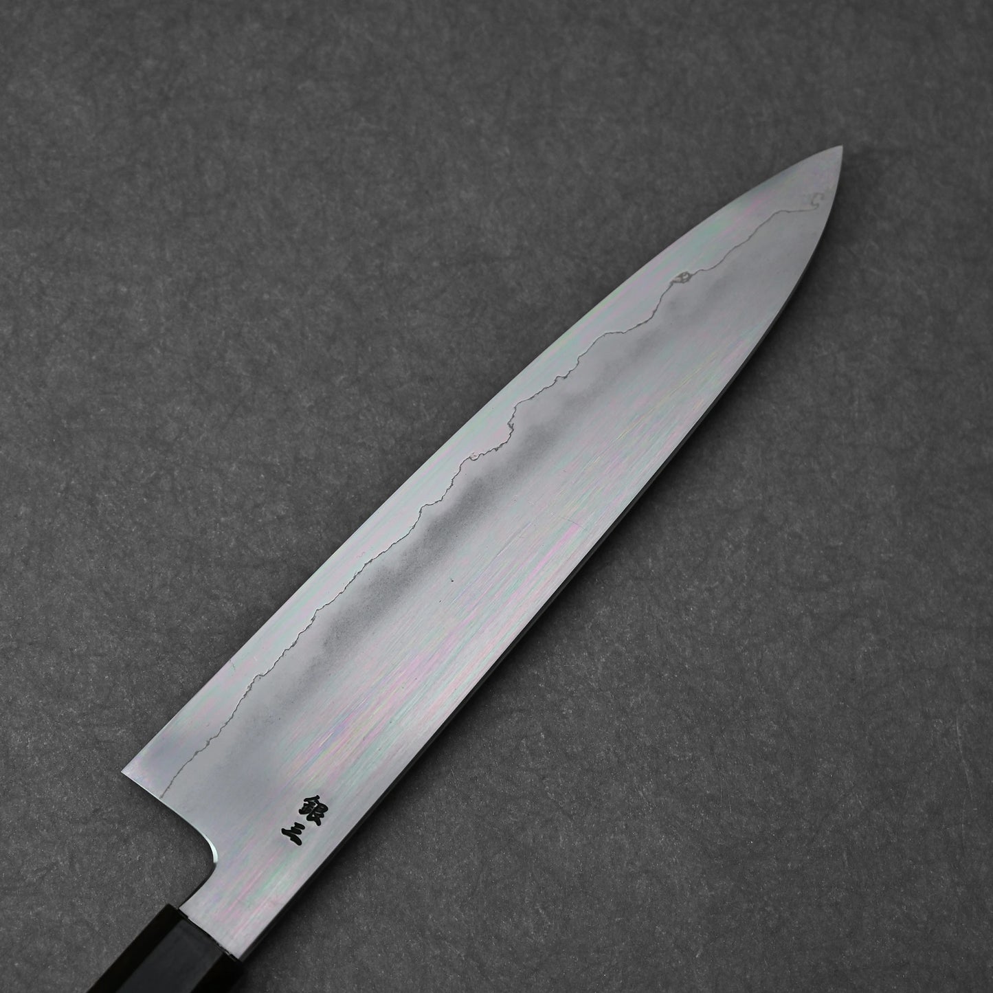 Close-up of the reverse side of a gyuto knife blade made with ginsan steel; photographed to highlight vertically engraved kanji characters and the polished steel finish.