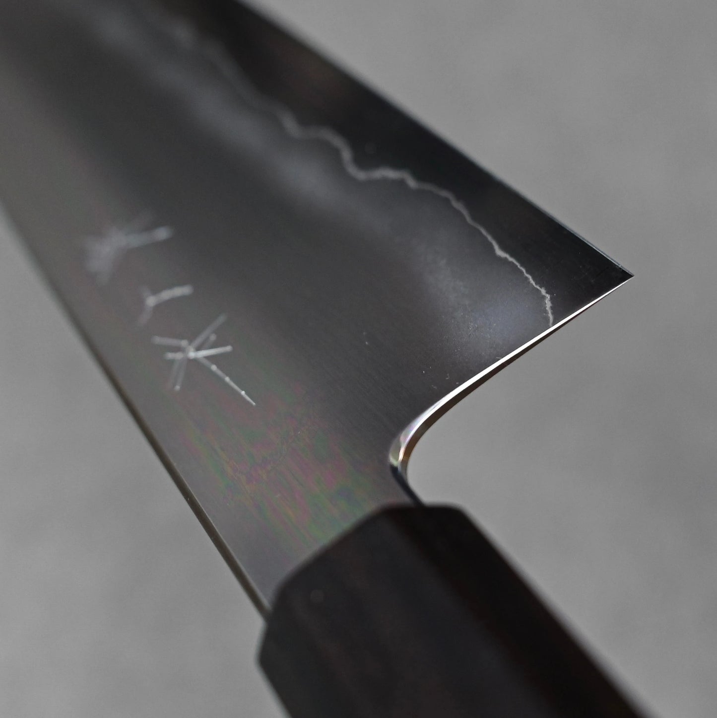 Close-up of a gyuto knife blade made with ginsan steel; photographed to emphasize the polished choil finish, grind transition, and steel texture near the handle.