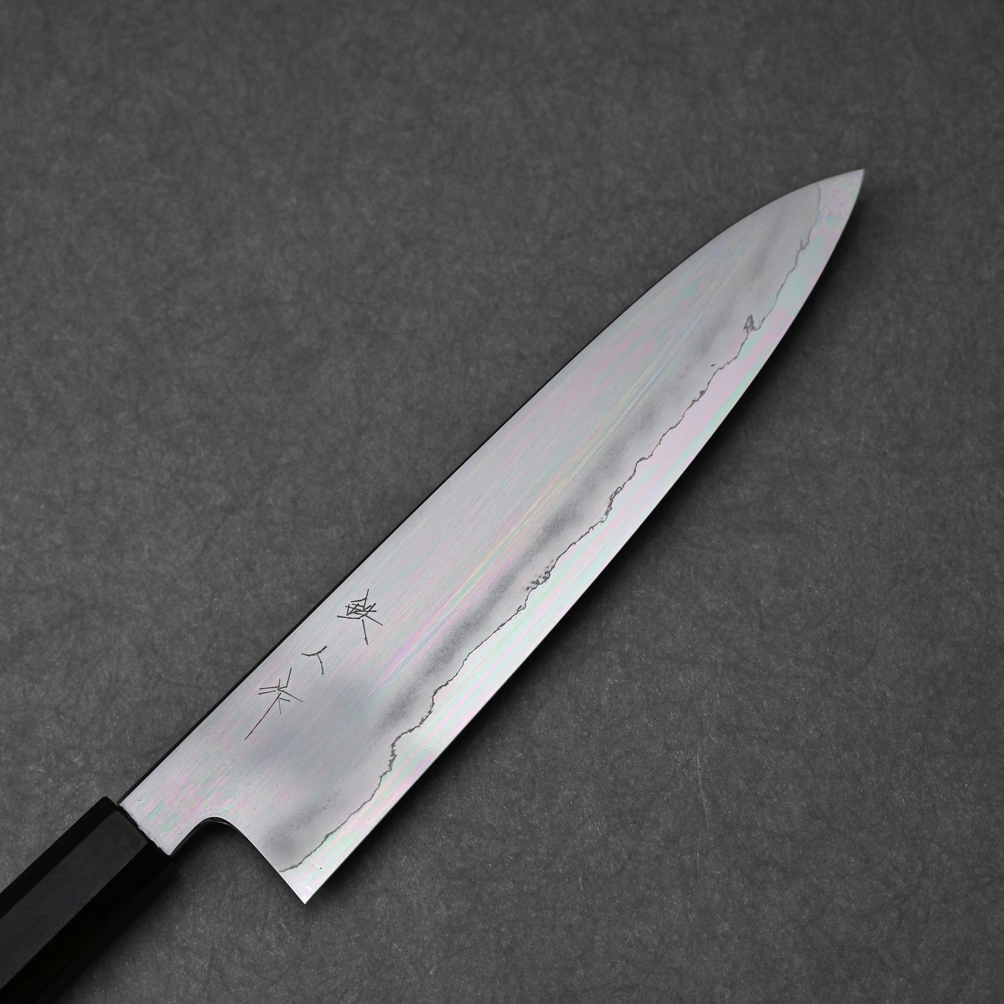 Close-up of a gyuto knife blade made with ginsan steel; photographed to clean finish, vertically engraved kanji characters, and polished steel finish.