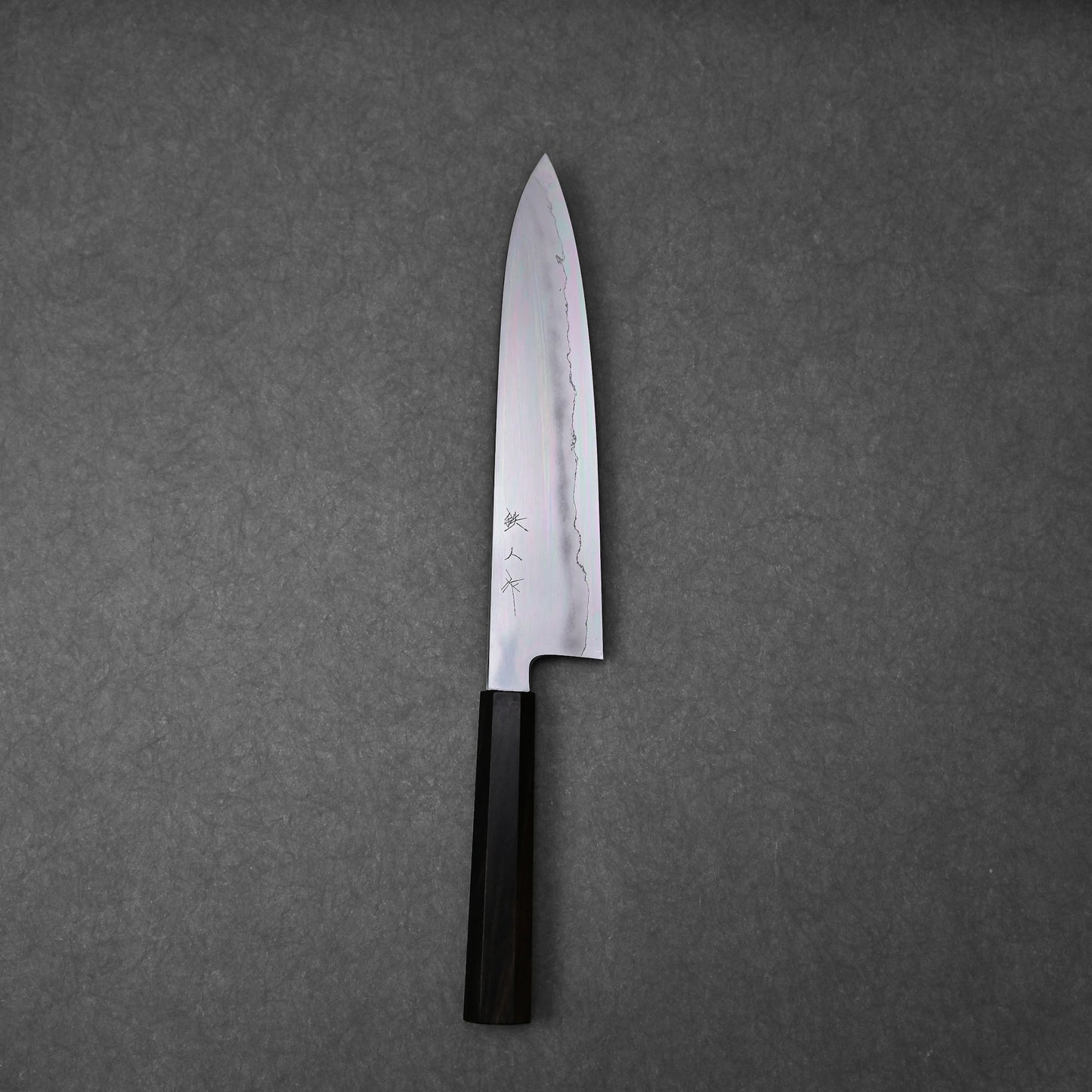 Gyuto knife made with ginsan steel; photographed in vertical orientation to show the full blade profile and handle, with visible hamon pattern and engraved kanji characters near the handle.
