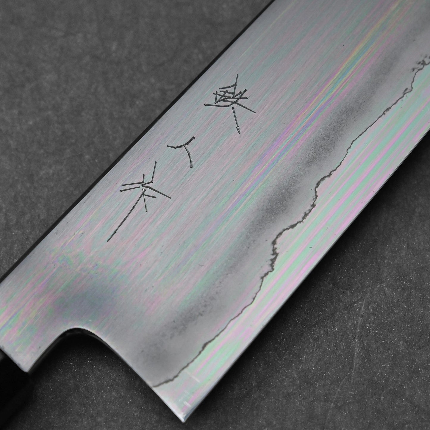 Close-up of a gyuto knife blade made with ginsan steel; photographed to highlight vertically engraved kanji characters and polished steel surface.