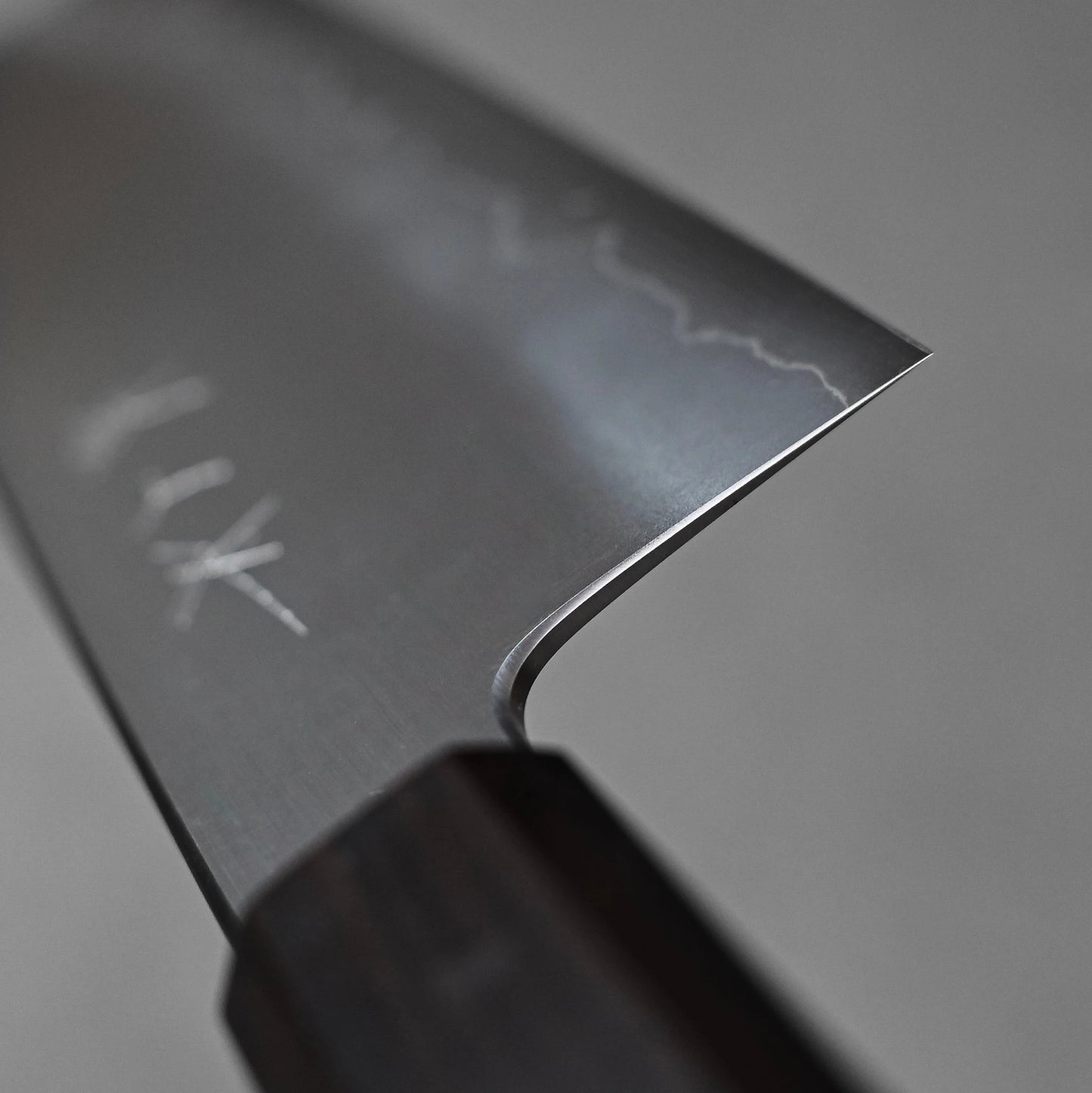 Close-up of a nakiri knife showing the choil finish near the handle; photographed to emphasize the precision, smoothness, and attention to detail in the grind and steel surface.