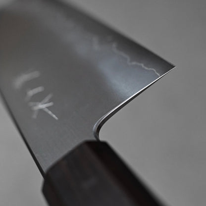 Close-up of a nakiri knife showing the choil finish near the handle; photographed to emphasize the precision, smoothness, and attention to detail in the grind and steel surface.