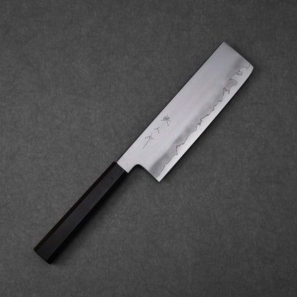 Nakiri knife with a rectangular blade featuring vertically engraved kanji near the spine; paired with a black octagonal handle and photographed flat against a textured surface to highlight the blade geometry and craftsmanship.