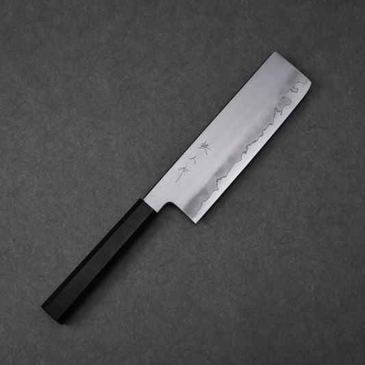 Nakiri knife with a rectangular blade featuring vertically engraved kanji near the spine; paired with a black octagonal handle and photographed flat against a textured surface to highlight the blade geometry and craftsmanship.