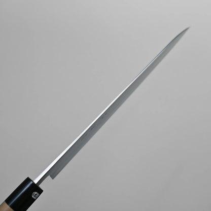Spine shot of a thin, long-bladed Sanjo gyuto kitchen knife held at an angle against a plain, light gray background. The blade appears sharp and tapers to a pointed tip.