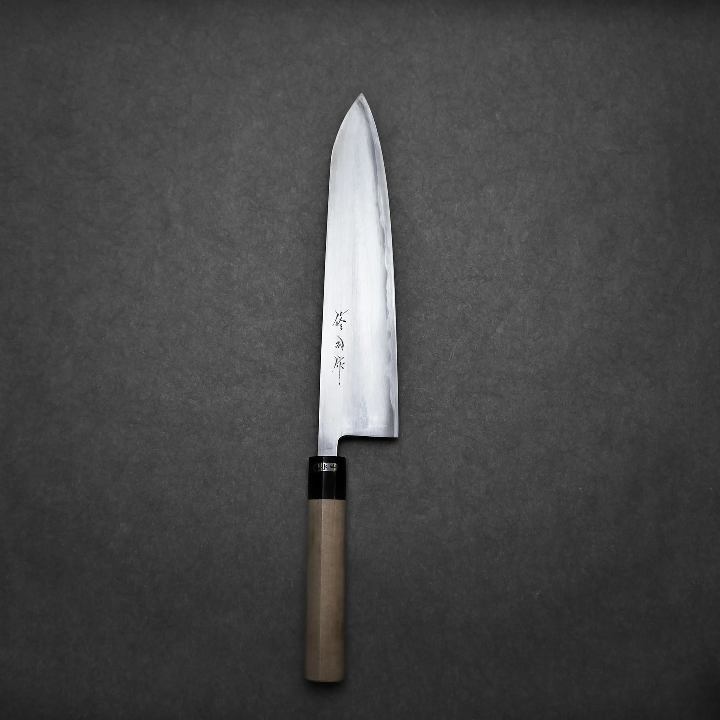 A single Sanjo gyuto chefs knife with a wooden handle and a sharp, silver blade featuring engraved characters, placed on a plain dark gray background.
