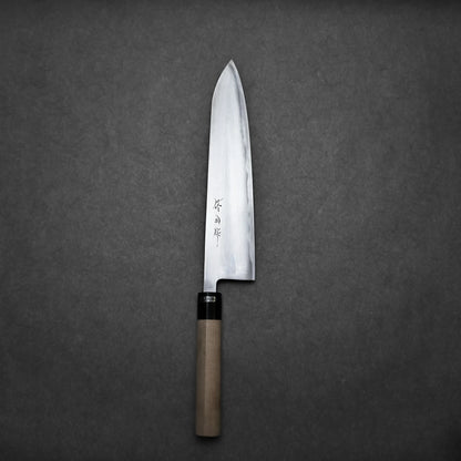 A single Sanjo gyuto chefs knife with a wooden handle and a sharp, silver blade featuring engraved characters, placed on a plain dark gray background.