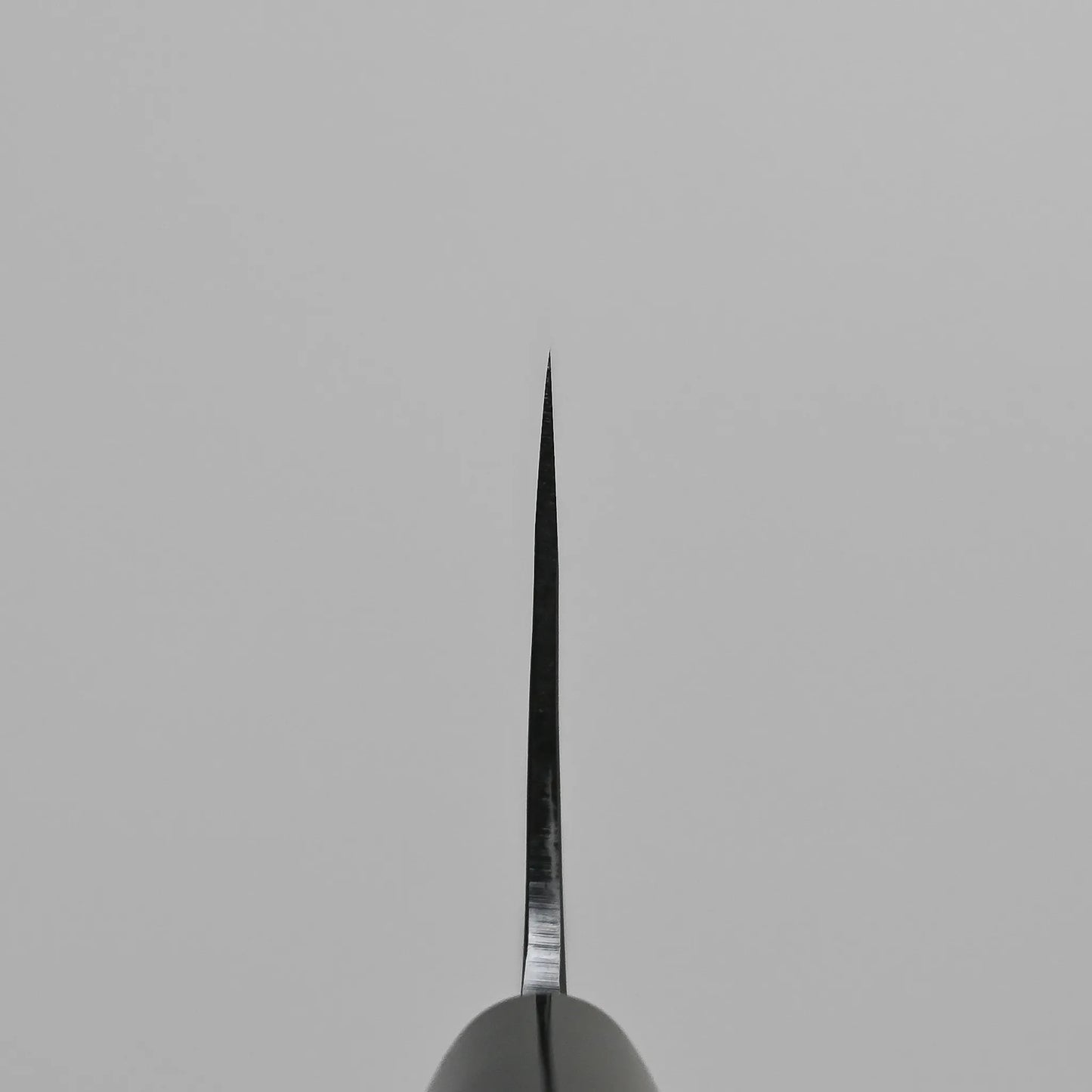 A choil shot of a kurouchi santoku knife blade against a plain, light gray background.