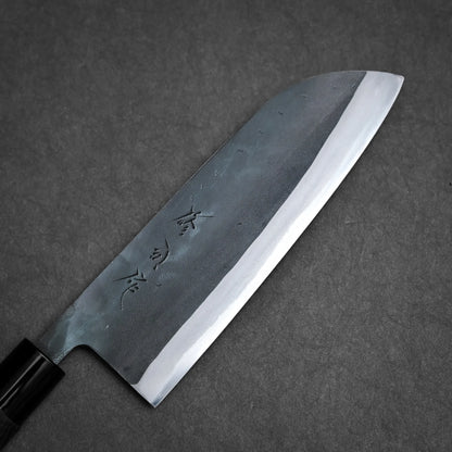 A Sanjo santoku Japanese-style kitchen knife with a dark handle and wide, sharp blade etched with Japanese characters, positioned on a textured gray surface.