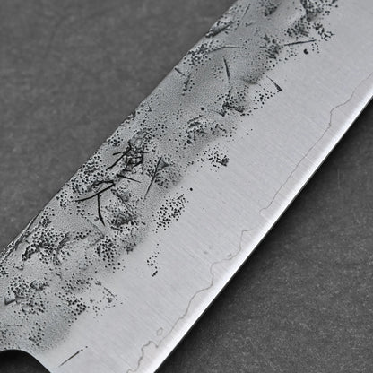 A close-up of the Tsunehisa nashiji SLD bunka 170mm blade highlights intricate nashiji patterns and fine lines on the SLD steel, with visible dark etching, set against a plain dark background.