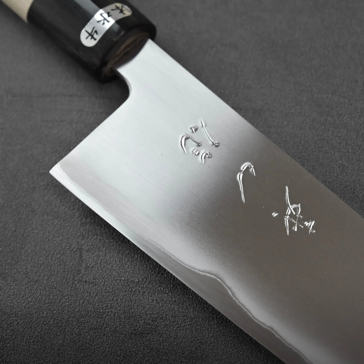 Gyuto with a dark wooden handle, metal bolster, and Japanese characters on the blade.
