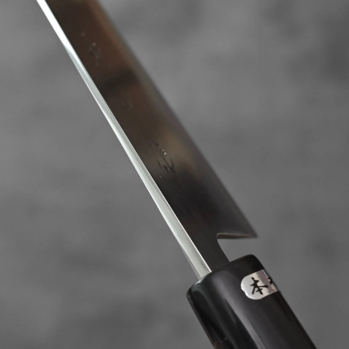 Gyuto with an engraved blade and a dark handle featuring a Japanese text label.