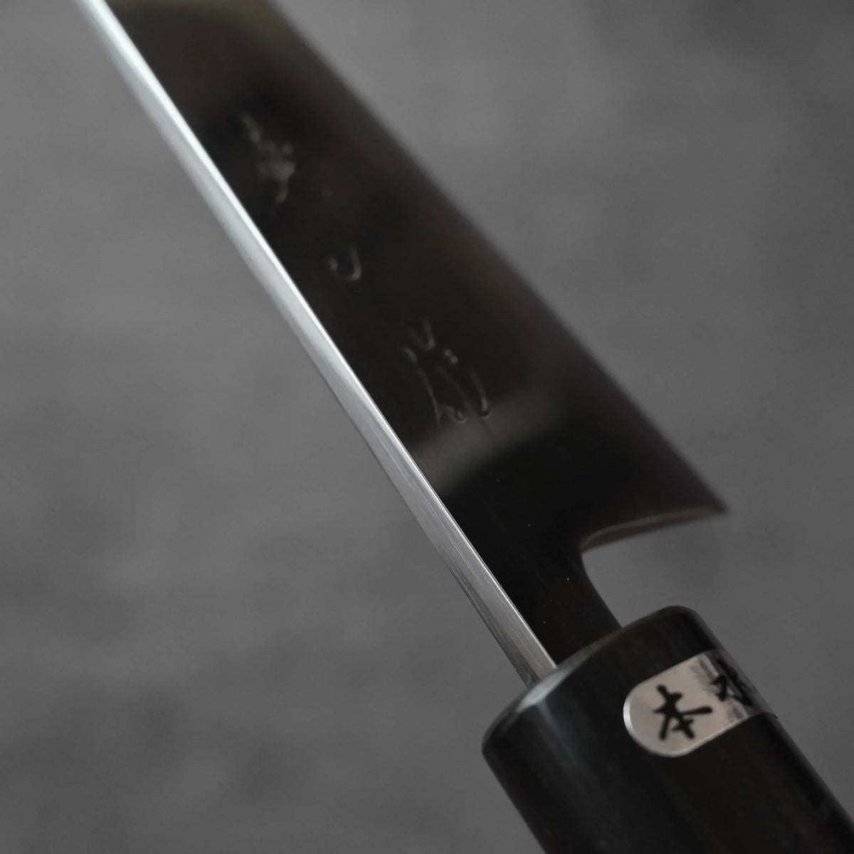 Honesuki with a dark, engraved blade and a black cylindrical handle.