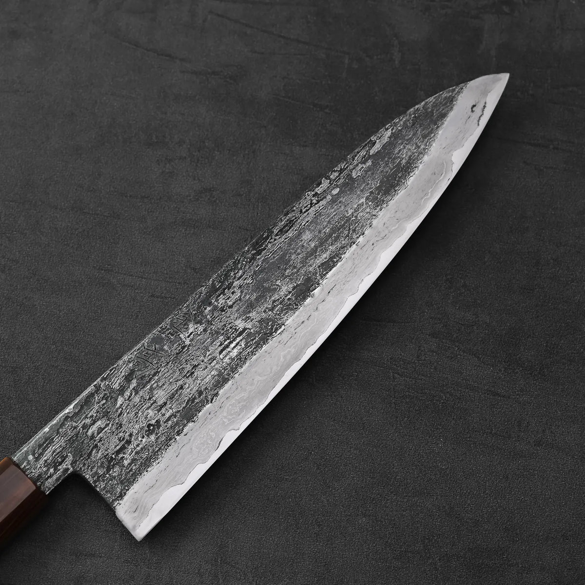 Gyuto with a textured blade and wrought iron cladding, shown in close-up highlighting its extra tall profile.