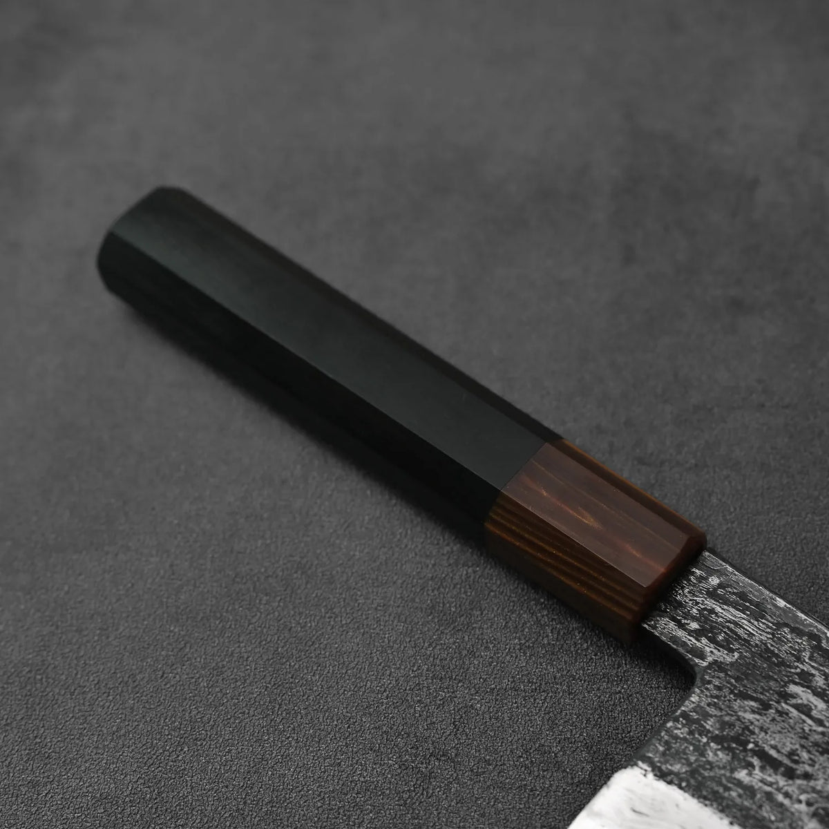Close-up of a gyuto knife’s black-brown wood handle and wrought iron cladding.