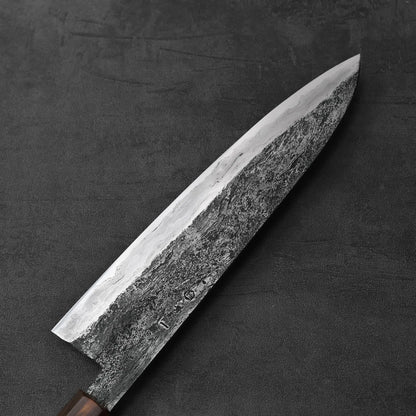 Close-up of a gyuto with a wood handle, highlighting the blade’s height and detailed metal texture.