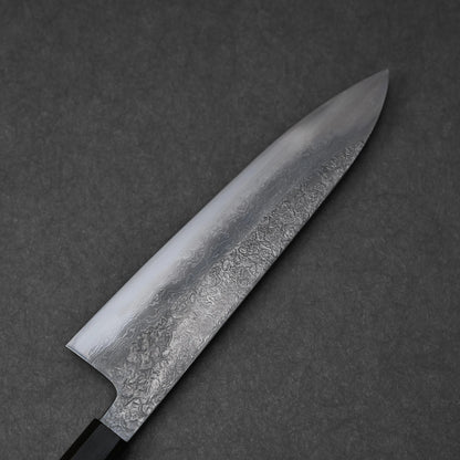 Reverse side of a Japanese knife blade featuring damascus steel patterns with layered waves and subtle forging marks; photographed close-up to highlight craftsmanship and steel texture.