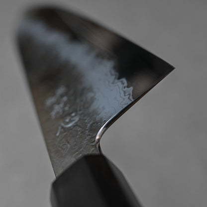 Close-up of a Japanese knife showing the choil area with a polished finish and subtle damascus steel wave patterns; photographed to emphasize edge detailing and craftsmanship near the handle transition.