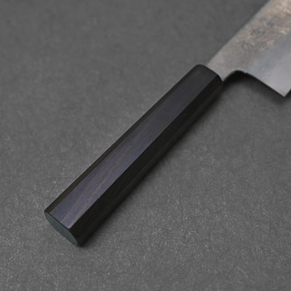 Handle of a Japanese knife featuring a dark octagonal shape with a smooth polished finish; photographed close-up against a textured dark surface to emphasize material quality and craftsmanship detail.