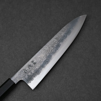 Japanese chef’s knife with damascus steel blade featuring layered forge patterns and vertically engraved kanji near the handle; paired with a black octagonal handle and photographed against a dark textured background.