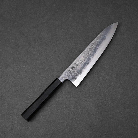 Japanese chef’s knife with a damascus steel blade featuring layered forge patterns and vertically engraved kanji near the handle; paired with a black octagonal handle and photographed on a dark textured surface.