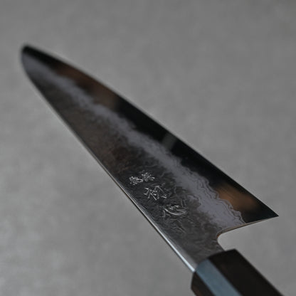 Close-up of a Japanese knife blade featuring damascus steel patterns with layered wave textures and vertically engraved kanji near the handle; photographed to highlight fine craftsmanship and artistic detail.