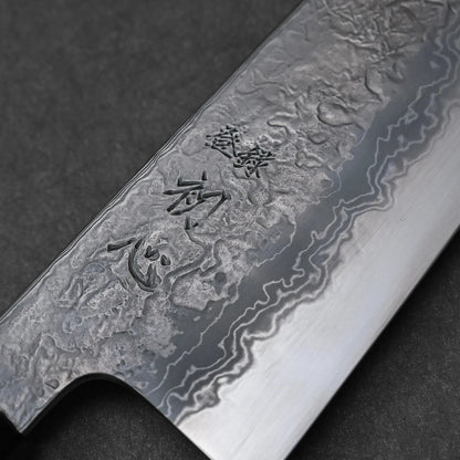 Close-up of a Japanese knife blade featuring damascus steel patterns with vertically engraved kanji characters near the spine; photographed to emphasize the blade’s layered texture and traditional artistry.