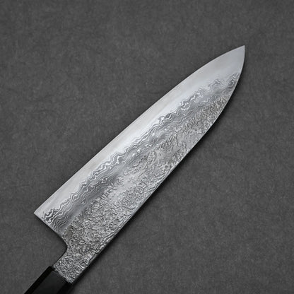 A close-up of the Yoshihide Masuda aogami#1 damascus santoku 180mm knife, featuring a Damascus finish blade with intricate wavy patterns and a textured appearance against a gray background.