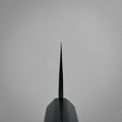 Choil shot of a tall gyuto knife blade, pointed directly upward against a plain, light gray background. The image emphasizes the thinness and precision of the blade’s edge.