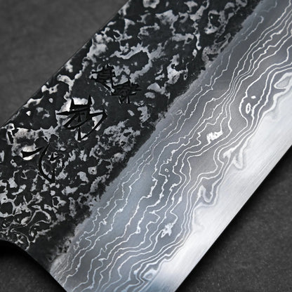 Close-up of a tall gyuto knife blade showing intricate Damascus steel patterns and engraved kanji characters on the textured upper part of the blade.