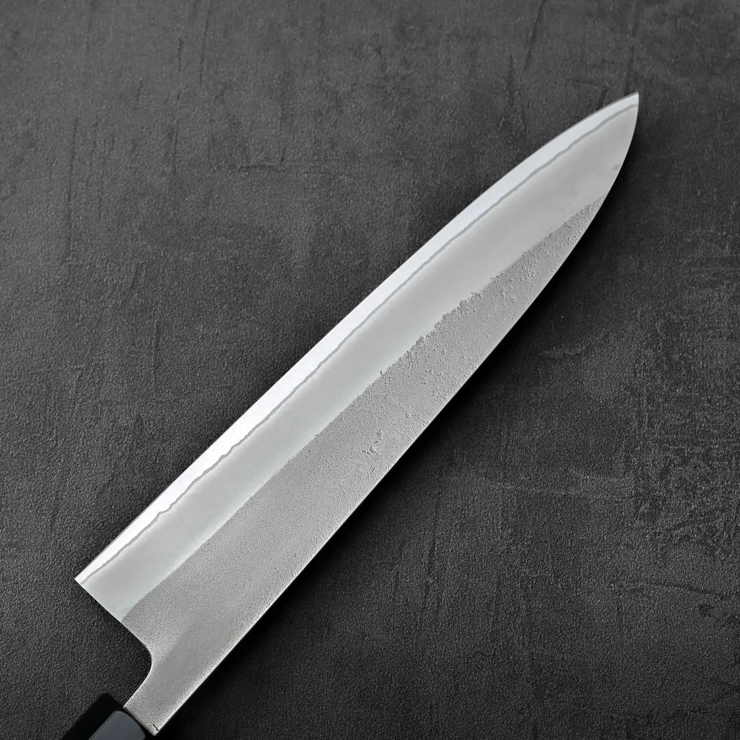 Close-up of a gyuto featuring visible nashiji finish and shirogami#2 steel, focus on blade detail.