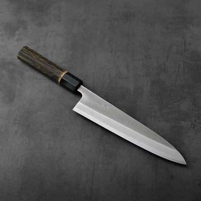 A gyuto with a burnt chestnut handle is shown, highlighting the grain of the wood and textured finish on the blade.