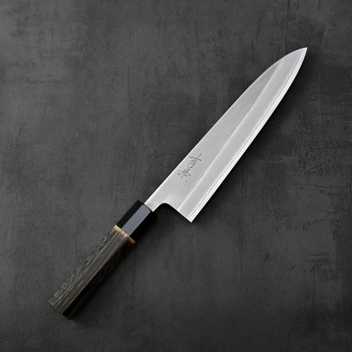 A Yoshikane nashiji shirogami#2 gyuto 210mm with a burnt chestnut handle is displayed, highlighting its shape and wood grain handle.