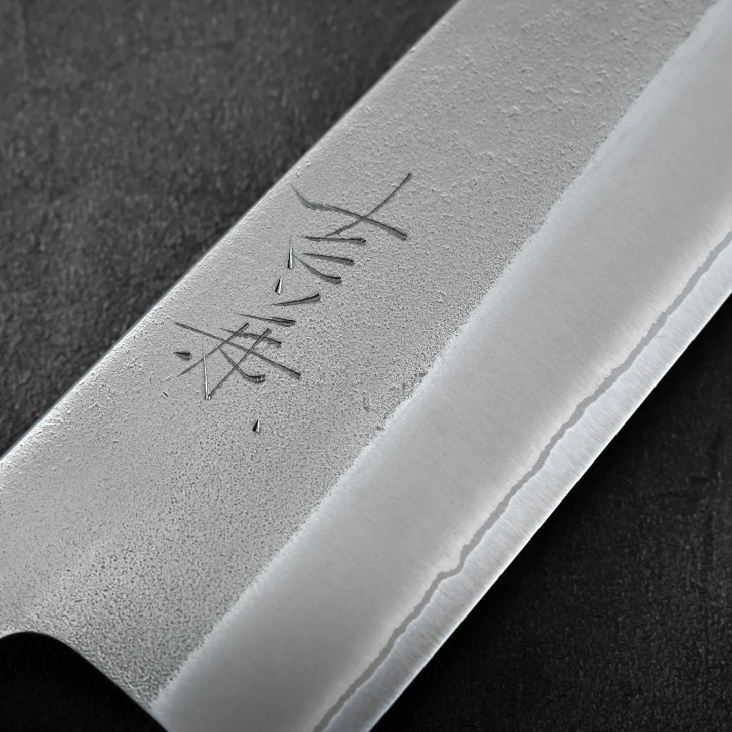 Close-up of a blade featuring kanji and nashiji finish, highlighting the distinct shape of a gyuto.