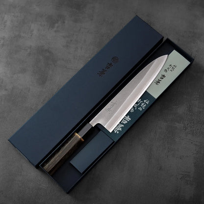 A gyuto with a burnt chestnut handle rests in a blue box, highlighting the contrast of materials and color.
