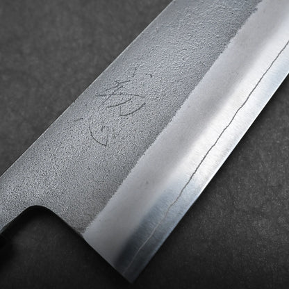 Close-up of a bunka knife blade with a visible hamon line and engraved Japanese characters, showing texture and detail of the metal against a dark background—an exquisite example of a compact all-purpose Japanese knife.