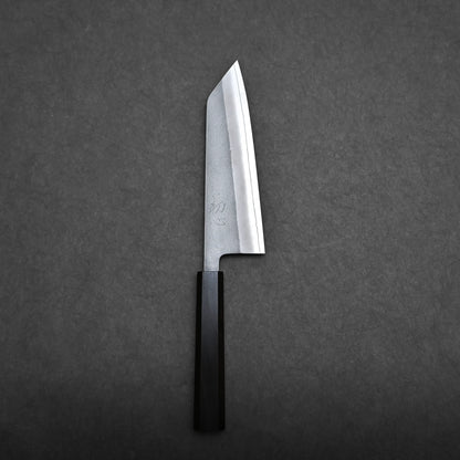 A compact all-purpose Japanese knife with a rectangular wooden handle and an angled, broad blade is placed on a dark grey textured surface, resembling the classic bunka knife style.