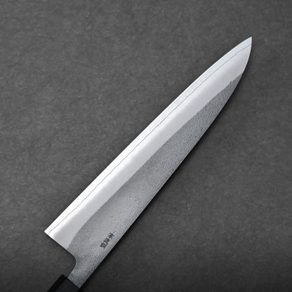 A close-up view of a Japanese chef's knife, or gyuto knife, with a sharp, shiny blade and a black handle, set against a dark gray textured background.