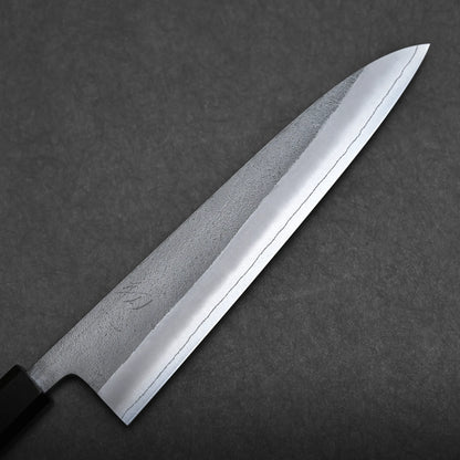 A close-up of a Japanese chef's knife with a sharp, polished blade and a dark handle, displayed against a textured dark gray background.