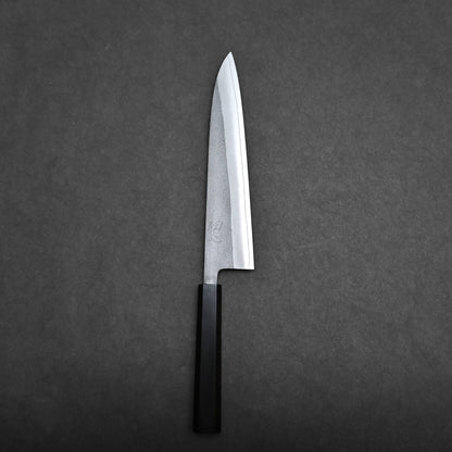 A single gyuto knife with a straight-edged blade and a black handle is placed on a dark gray surface, photographed from above.